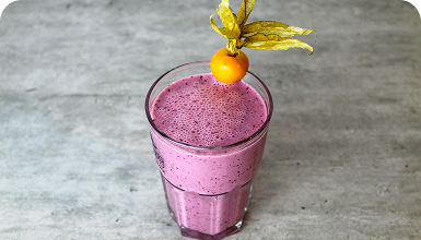 Ein Glas mit lila Smoothie, garniert mit einer Physalis und einem Blatt.