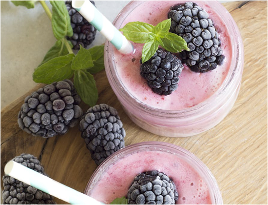 Zwei Gläser mit Beeren-Smoothie, garniert mit Minze und frischen schwarzen Beeren, auf einem Holzbrett.