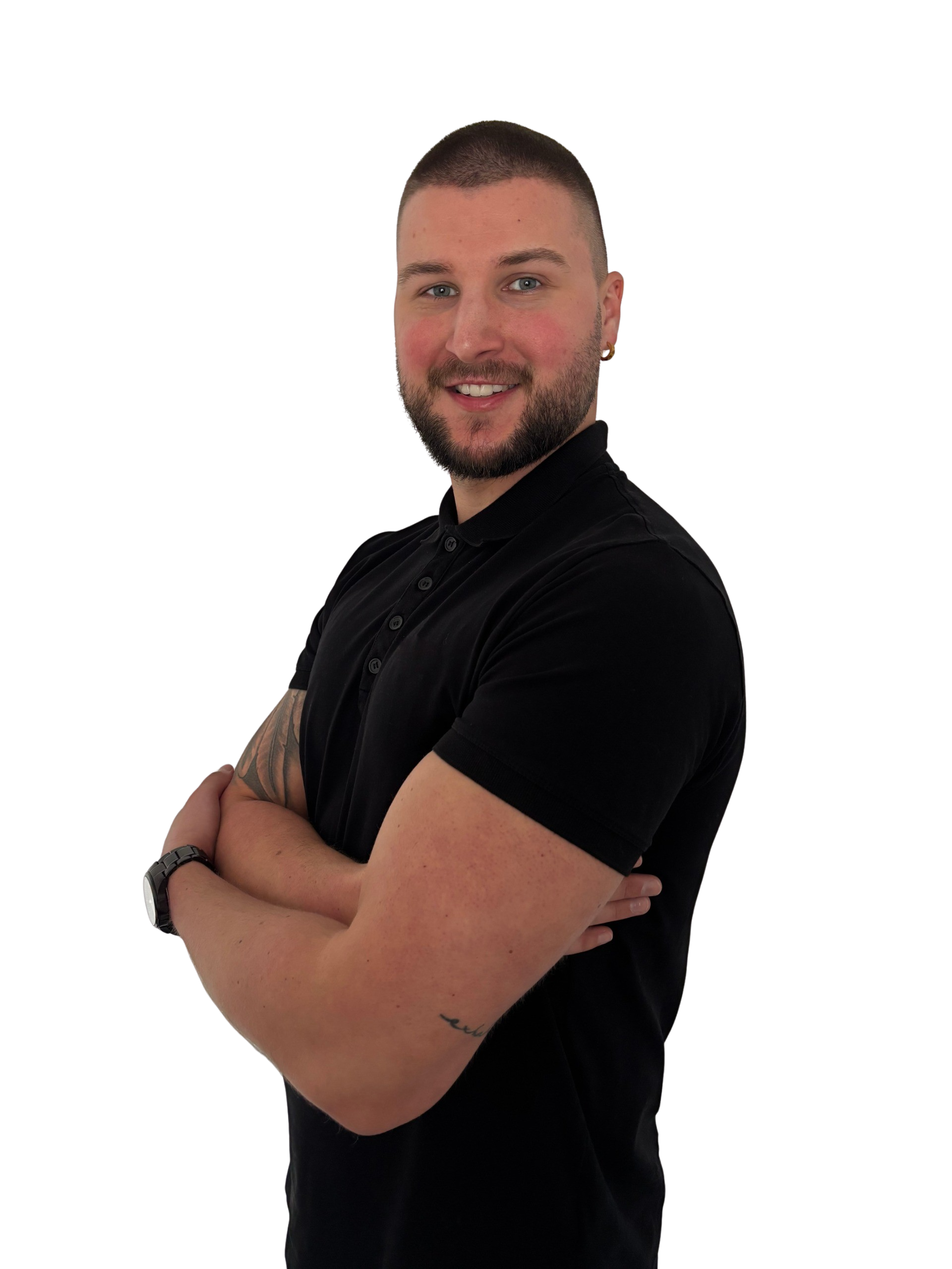 Junger Mann mit kurzem Bart und Kreuz-Armhaltung, trägt ein schwarzes Poloshirt, vor schwarzem Hintergrund.